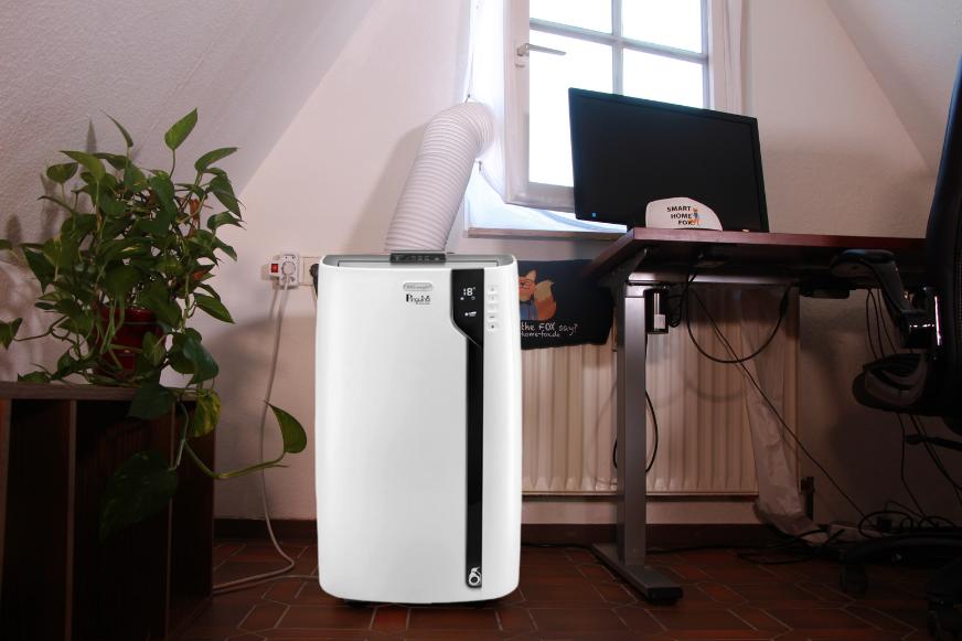 Die De’Longhi mobile Klimaanlage steht direkt unter einem Fenster und der Abluftschlauch geht durch die Fensterabdichtung nach draußen.